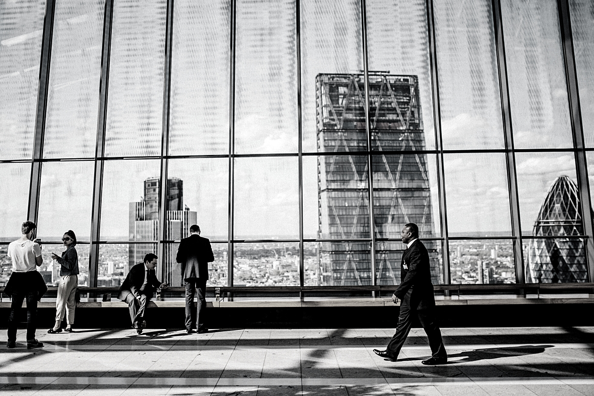 Man Walking on Sidewalk Near People Standing and Sitting Beside Curtain-wall Building